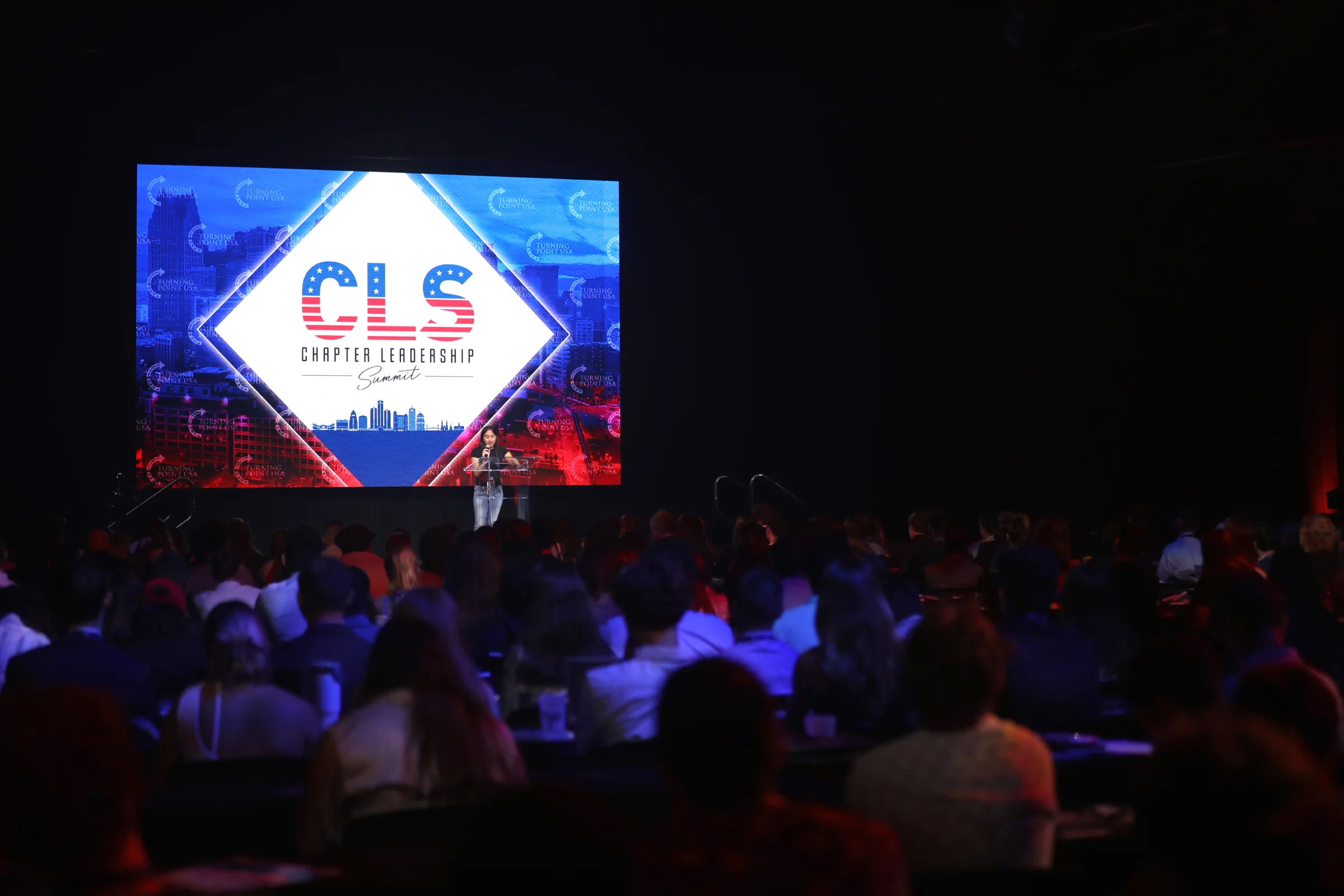 Chloe Cole speaking to a large live audience from a stage