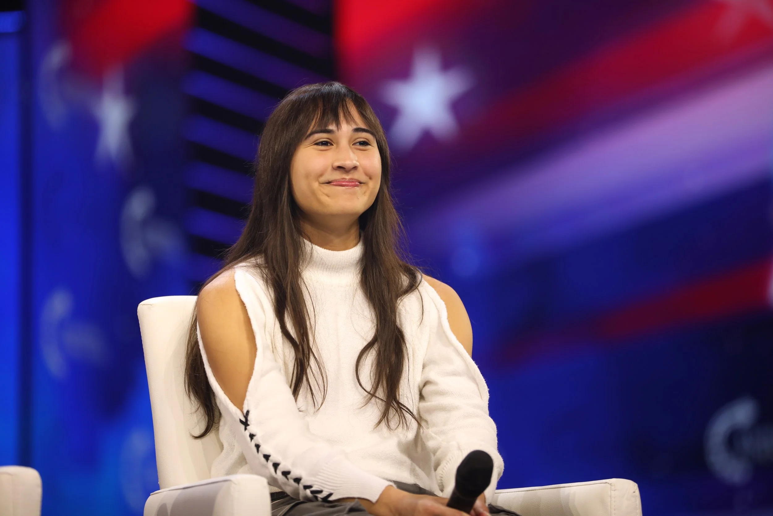 Chloe Cole smiling while seated on a live event stage