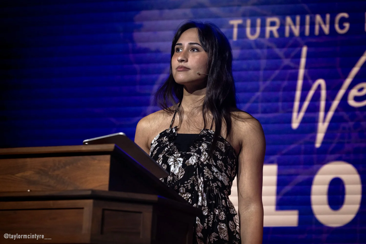 Chloe Cole delivering remarks from a podium on a blue-lit stage
